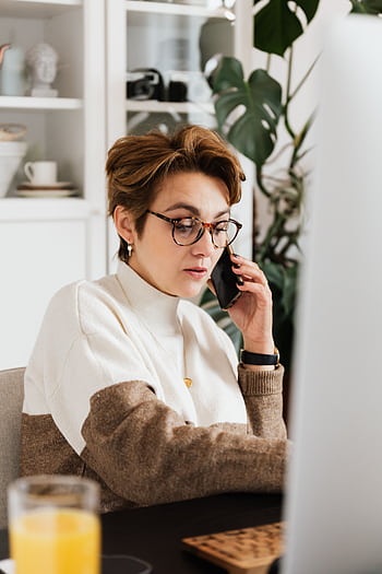 Elegant businesswoman with glasses talking on a smart in a modern office, focused and professional. HD phone wallpaper