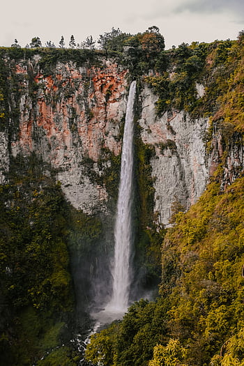 Breathtaking view of Sipiso-piso Waterfall cascading amidst lush greenery in North Sumatra, Indonesia. HD phone wallpaper
