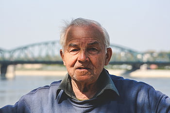 Portrait of an elderly man with gray hair in front of a scenic bridge on a bright day. HD wallpaper