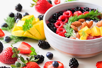 A vibrant bowl filled with fresh berries, mango, almonds, and herbs, perfect for a healthy snack or breakfast. HD wallpaper