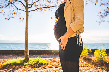 Expectant mother embracing nature during a fall day by the ocean. HD wallpaper