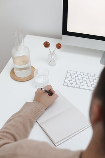 A person writing in a notebook at a modern minimalist workspace with a computer. HD phone wallpaper
