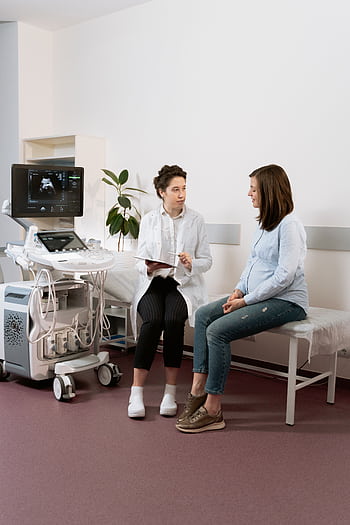 Healthcare professional consulting with a pregnant patient in a medical clinic using ultrasound equipment. HD phone wallpaper