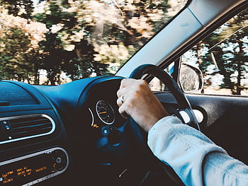 Driver's hand on steering wheel of a modern car during a daytime drive through scenic outdoors. HD wallpaper
