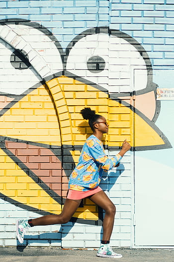 Dynamic scene of a woman running against a colorful graffiti wall, capturing urban art energy. HD phone wallpaper