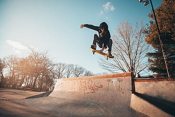 A skateboarder performs an aerial trick at a skate park on a sunny day, displaying skill and agility. HD wallpaper