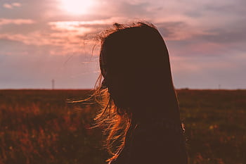 Artistic silhouette of a woman with flowing hair against a beautiful sunset in a field. HD wallpaper