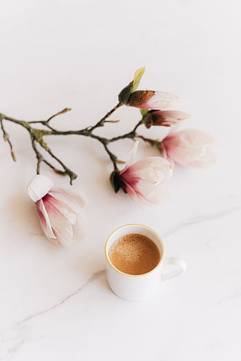 Delicate magnolia flowers with a fresh cup of coffee on a marble surface, evoking a peaceful morning vibe. HD phone wallpaper