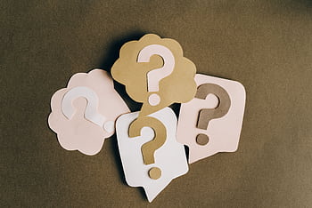 Four paper cutouts of question marks in beige and white on a brown surface, symbolizing inquiry and curiosity. HD wallpaper