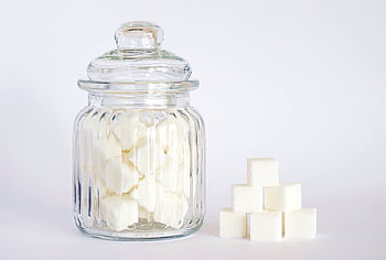 A clear glass jar filled with sugar cubes next to stacked cubes on a white background. HD wallpaper