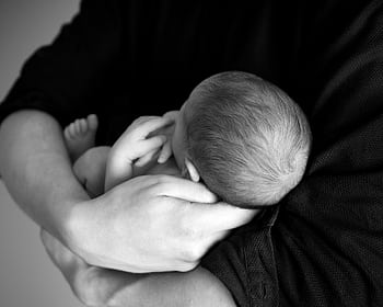 A black and white close-up of a parent holding a newborn baby in arms, conveying love and care. HD wallpaper