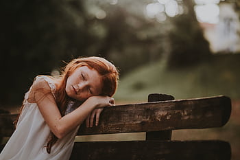 A young girl sleeps peacefully on a wooden bench outdoors, surrounded by nature. HD wallpaper