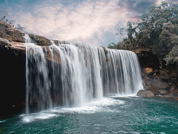 Peaceful waterfall cascading over rocks with lush forest backdrop and serene sky. HD wallpaper