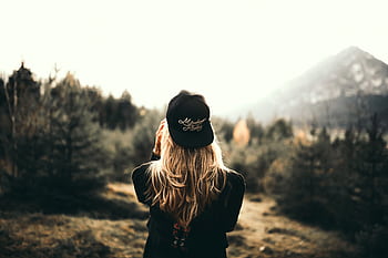 A woman in black cap and sweater enjoys a mountain view, embracing outdoor adventure. HD wallpaper