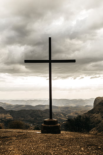 A powerful silhouette of a cross set against a dramatic cloudy mountain landscape. HD phone wallpaper