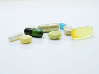 Close-up of various pills and capsules arranged on a white surface, representing healthcare and medicine. HD wallpaper