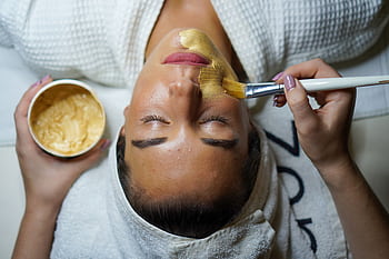 A woman enjoying a gold facial mask for relaxation and skincare at a spa. HD wallpaper