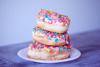 A stack of doughnuts covered in colorful fruity pebbles on a plate. HD wallpaper