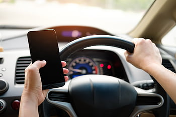 A driver uses a smart while steering a vehicle, showcasing distracted driving risks. HD wallpaper