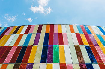 A colorful glass facade with vertical stripes under a bright blue sky, showcasing modern architecture. HD wallpaper