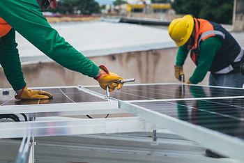 Workers secure solar panels on a rooftop, advancing renewable energy. HD wallpaper