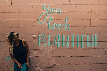 A stylish woman with curly hair and sunglasses poses beside a vibrant mural in Toronto. HD wallpaper