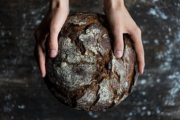 Close-up of hands holding a rustic loaf of whole wheat bread with a dark, textured crust. HD wallpaper