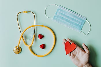 Flat lay of medical tools with a stethoscope, mask, and heart shapes representing healthcare essentials. HD wallpaper