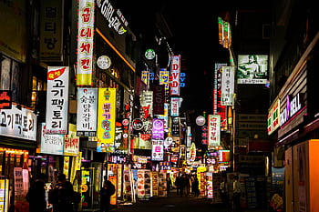 Explore Seoul's vibrant nightlife on a bustling neon-lit street lined with shops and restaurants. HD wallpaper