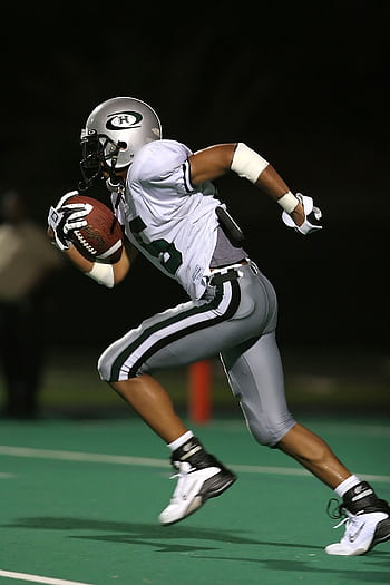 High-speed capture of a football player running on the field during a night game, showcasing athleticism. HD phone wallpaper