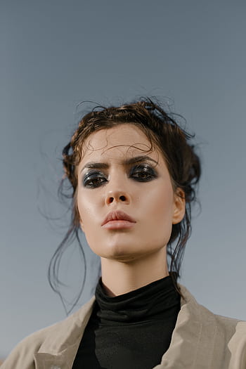 Stunning portrait of a model with bold eyeshadow and styled hair against a clear sky backdrop. HD phone wallpaper