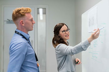 Two colleagues engaged in an office discussion at the whiteboard. HD wallpaper