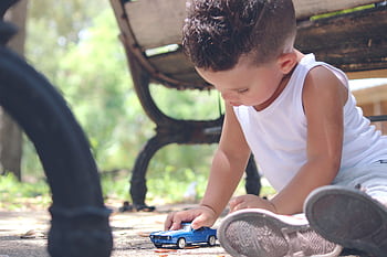 A young boy engaged in imaginative play with a toy car in a sunny park setting. HD wallpaper