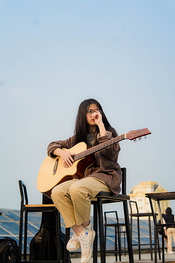 A woman sitting on a chair playing guitar at sunset in an outdoor setting. HD phone wallpaper