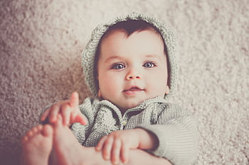 A cute baby in a knitted outfit lying on a soft carpet, smiling warmly. HD wallpaper
