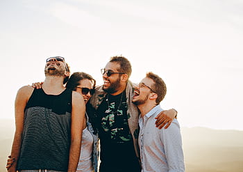 A group of young adults laughing and enjoying time together outdoors under the sun. HD wallpaper