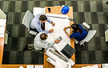 Top view of a team working on construction plans in an office setting. HD wallpaper