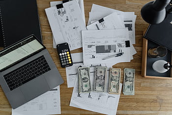 Overhead view of financial documents, cash, and technology on a wooden desk. HD wallpaper