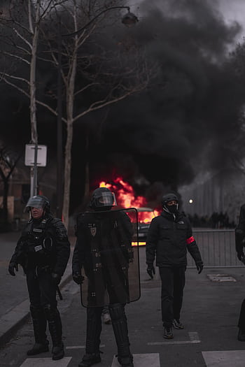 Riot police in gear confronting a street fire during an urban protest at night. HD phone wallpaper