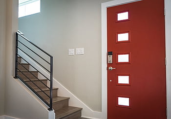 Contemporary interior with a vibrant red entrance door and stairs, showcasing minimalist design. HD wallpaper