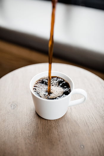 Steaming black coffee being poured into a white ceramic mug on a wooden table. HD phone wallpaper