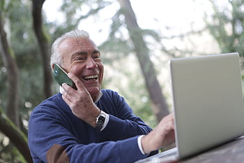 Happy senior man talking on and using laptop outdoors. HD wallpaper