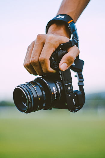 Close-up of a hand holding a vintage camera outdoors with a blurred green background, creating a bokeh effect. HD phone wallpaper