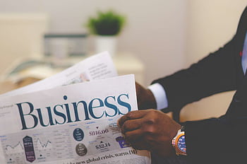 Close-up of a businessman reading a newspaper indoors, focusing on business headlines. HD wallpaper
