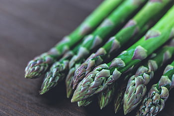 Close-up of fresh green asparagus spears displayed on a rustic wooden table. HD wallpaper