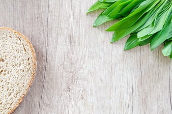 A slice of bread and fresh wild garlic leaves on a rustic wooden table. HD wallpaper