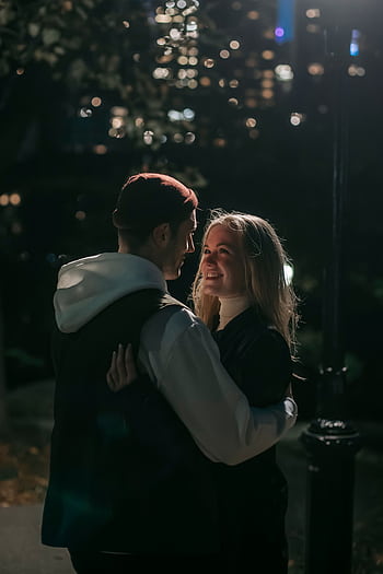A couple shares a tender embrace under city lights during a nighttime stroll in the park. HD phone wallpaper