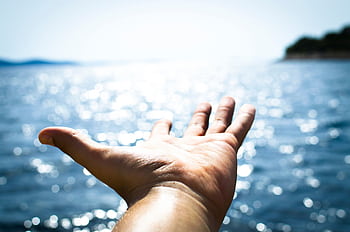 A hand reaching towards the sparkling sea, symbolizing dom and hope. HD wallpaper