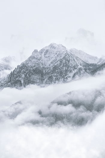 Breathtaking winter scene of a snow-covered mountain peak surrounded by misty clouds. HD phone wallpaper