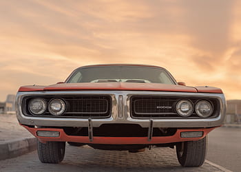 Front view of a classic Dodge muscle car under a vibrant sunset in Sharjah, UAE. HD wallpaper